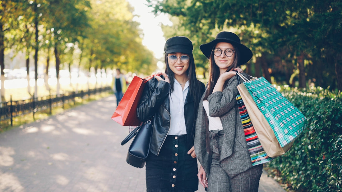 Two women with shopping bags in a park.